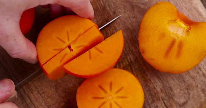 Half-ripe orange persimmon, fresh ripe persimmon cut into pieces on a cutting board with a sharp knife