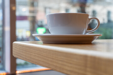 Tasty raf coffee in restaurant on city ​​life background. Still life white cup with hot drink on wooden platform. Coffee steamed and whipped cream with crushed chocolate. Relaxation on terrace in cafe