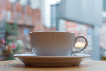Tasty raf coffee in restaurant on city ​​life background. Still life white cup with hot drink on wooden platform. Coffee steamed and whipped cream with crushed chocolate. Relaxation on terrace in cafe