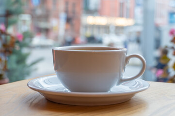 Tasty raf coffee in restaurant on city ​​life background. Still life white cup with hot drink on wooden platform. Coffee steamed and whipped cream with crushed chocolate. Relaxation on terrace in cafe