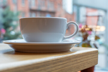 Tasty raf coffee in restaurant on city ​​life background. Still life white cup with hot drink on wooden platform. Coffee steamed and whipped cream with crushed chocolate. Relaxation on terrace in cafe