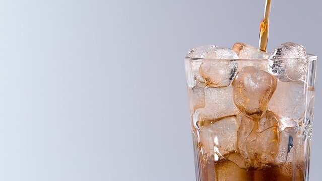 Pouring cola drink with ice cubes close-up. Fizzing cola with ice in glass. Refreshing tasty cola drink.