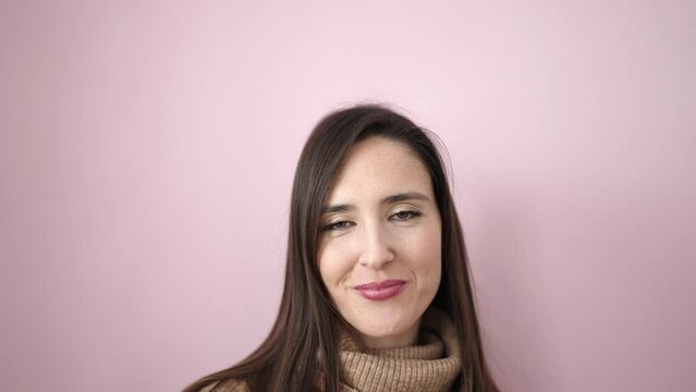 Beautiful hispanic woman standing with surprise expression looking up over isolated pink background
