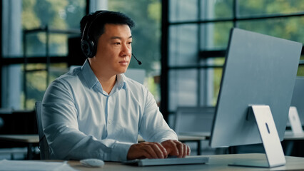 Asian businessman man consultant adviser teacher in headphones work at helpline company support client distant by video chat in office tell online course of business strategy telemarketing profession