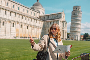 Young female traveler with tourist map near the famous leaning tower in Pisa old town. Happy vacations in Italy. High quality photo