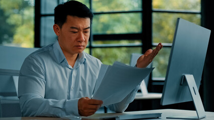 Desperate sad asian japanese senior specialist businessman sit at office read documents scam...