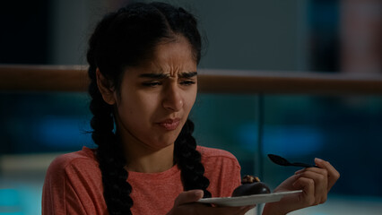 Arabian young woman client eat musty chocolate cake with teaspoon distasteful spoiled brownie in...