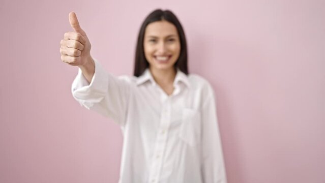 Young beautiful hispanic woman smiling confident doing ok sign with thumb up over isolated pink background