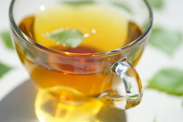 Green tea in a glass cup with a birch leaf. Leaves on a white table around a mug with a drink