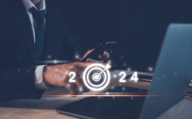 2024 business planning and strategy concept, businessman pointing virtual icon of the year 2024 target darts working on computer, phone, marketing financial analysis, investment trends next new year