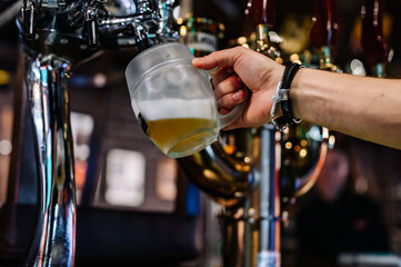man bartender hand at beer tap pouring beer in glass in bar or pub