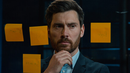Thoughtful Caucasian businessman employee middle-aged man analyze information on stickers read sticky notes on glass wall standing in office planning project manage tasks startup ideas organizes work - Powered by Adobe