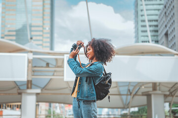 Happy young tourist African American woman taking photos with mirrorless camera on street in the city, Tourist journey trip concept