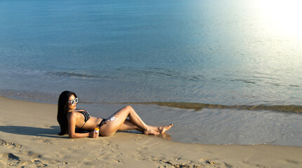 Sexy Asian woman in swimming costume with sun protection cream. protecting skin with sunblock cream from UV at summer tropical beach