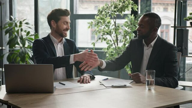 Two diverse businessmen at office meeting shake hands after successful business contract agreement. African businessman signing paper document offer Caucasian man salesman handshake client customer