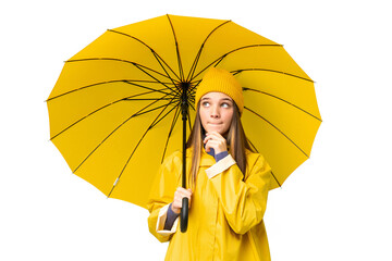 Teenager girl with rainproof coat and umbrella over isolated chroma key background having doubts...