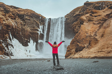 Happy tourist traveler woman enjoying with open arms on Skogafoss waterfall in Iceland, Europe...