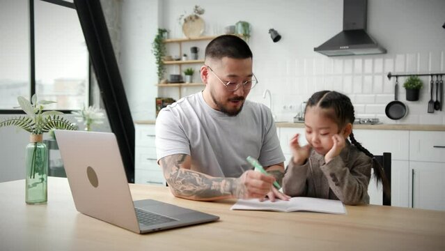 Young Father Helping Kid with Online Schooling. Asian family doing school homework together sitting at home.