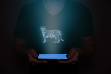 A young man from the future holds a smartphone onto which a tiger is projected. Future technology.