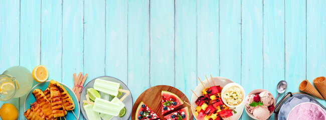 Refreshing summer food bottom border. Selection of grilled fruits, ice cream and ice pops. Top view on a blue wood banner background.