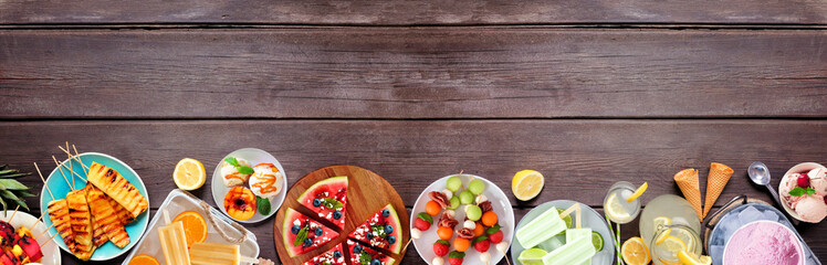 Refreshing summer food bottom border. Collection of grilled fruits, ice cream and ice pops. Top down view on a dark wood banner background.
