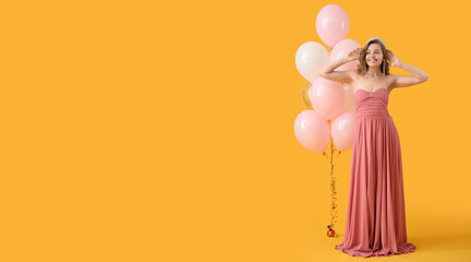 Beautiful young woman in prom dress and with balloons on yellow background with space for text