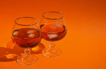a glass with cognac and pieces of people, an alcoholic drink on an orange background.