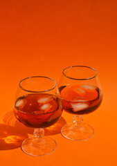 a glass with cognac and pieces of people, an alcoholic drink on an orange background.