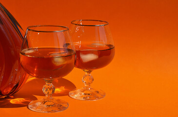 a glass with cognac and pieces of people, an alcoholic drink on an orange background.