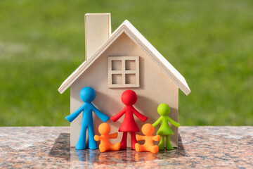 Miniature wooden house and symbolic figurines of a traditional family with three children against the backdrop of a sunlit lawn