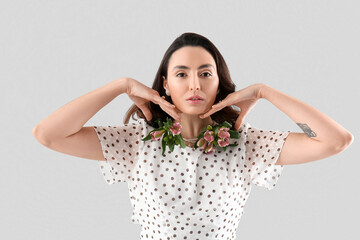 Young woman in dress with alstroemeria flowers on grey background