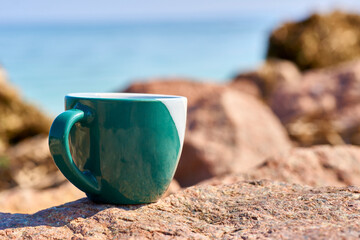 Fototapeta na wymiar Green ceramic cups for coffee tea beverages on the shore of a rocky sea bay
