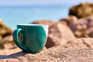 Foto op Plexiglas Camps Bay Beach, Kaapstad, Zuid-Afrika Green ceramic cups for coffee tea beverages on the shore of a rocky sea bay