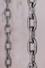 Two iron chains hang vertically on a light background. Iron traction structure. Steel chain. One by one. Male background. Parallel lines.