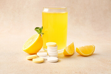 Glass of vitamin C effervescent tablet dissolved in water and lemons on beige grunge table