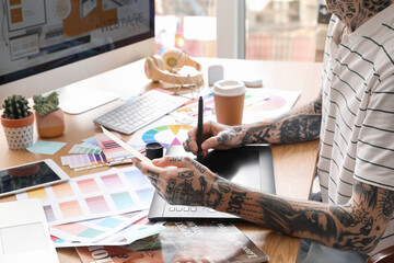 Tattooed graphic designer working with tablet and paint palette on table in office, closeup