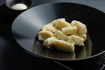 A bowl of gnocchi with a side of sour cream.