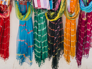 Multi-colored chiffon scarves hang on hangers along a white wall