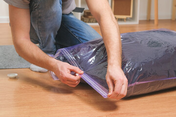 A man folds winter jackets and puts them in a vacuum bag for seasonal storage in the closet. Space saving and careful storage of clothes. Organization of storage.