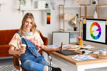 Female graphic designer with cup of coffee working at table in office