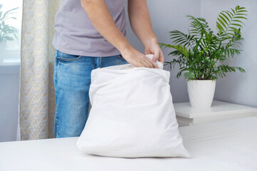 A man tucks a pillow with a fresh bright white pillowcase. Making the bed with fresh bed linen by a...