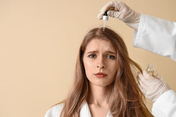 Naklejka premium Cosmetologist applying serum for hair growth on young woman against beige background, closeup