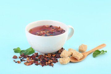 Glass of fruit tea, wooden spoon and snacks on blue background