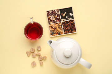Glass of tea, teapot, snacks and board with different fruit mixes on yellow background