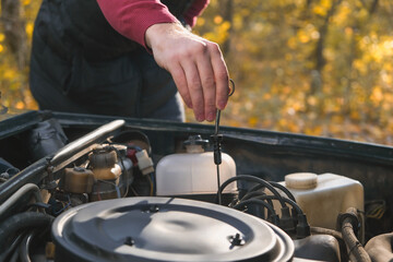 A man checks the oil level in the car engine. Self-service of the car. Periodic check of the oil level in the engine.