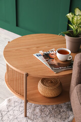 Coffee table with cup of tea, magazines and houseplant near armchair in living room
