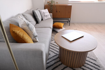 Modern laptop on coffee table near grey sofa in stylish living room