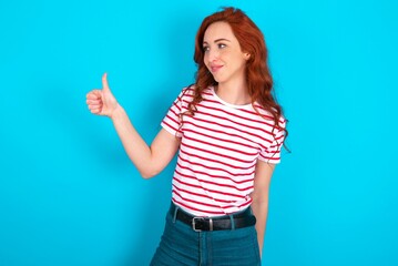 young redhead woman wearing striped T-shirt over blue background Looking proud, smiling doing...