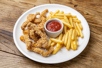 A plate of chicken nuggets with french fries and ketchup on a wooden table.