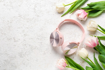 Modern headphones with beautiful tulip flowers on light background